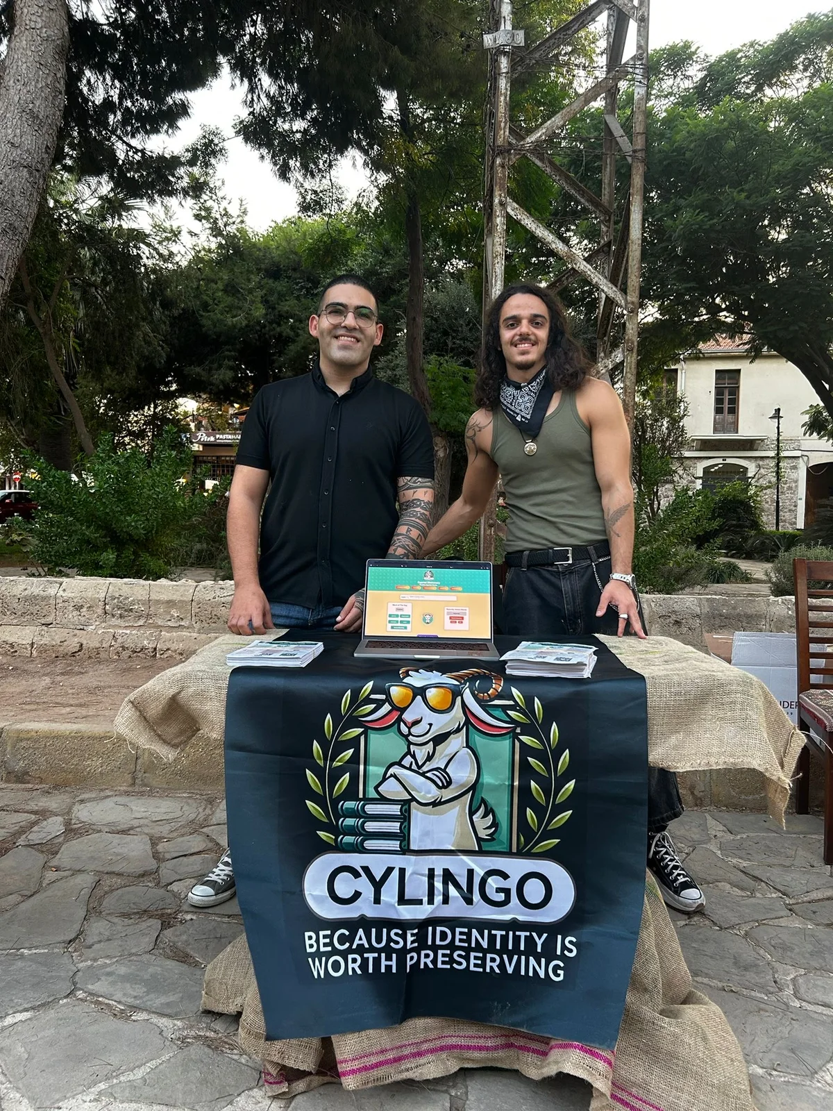Cylingo representatives at their outdoor festival table in Famagusta with a laptop, leaflets and banner
